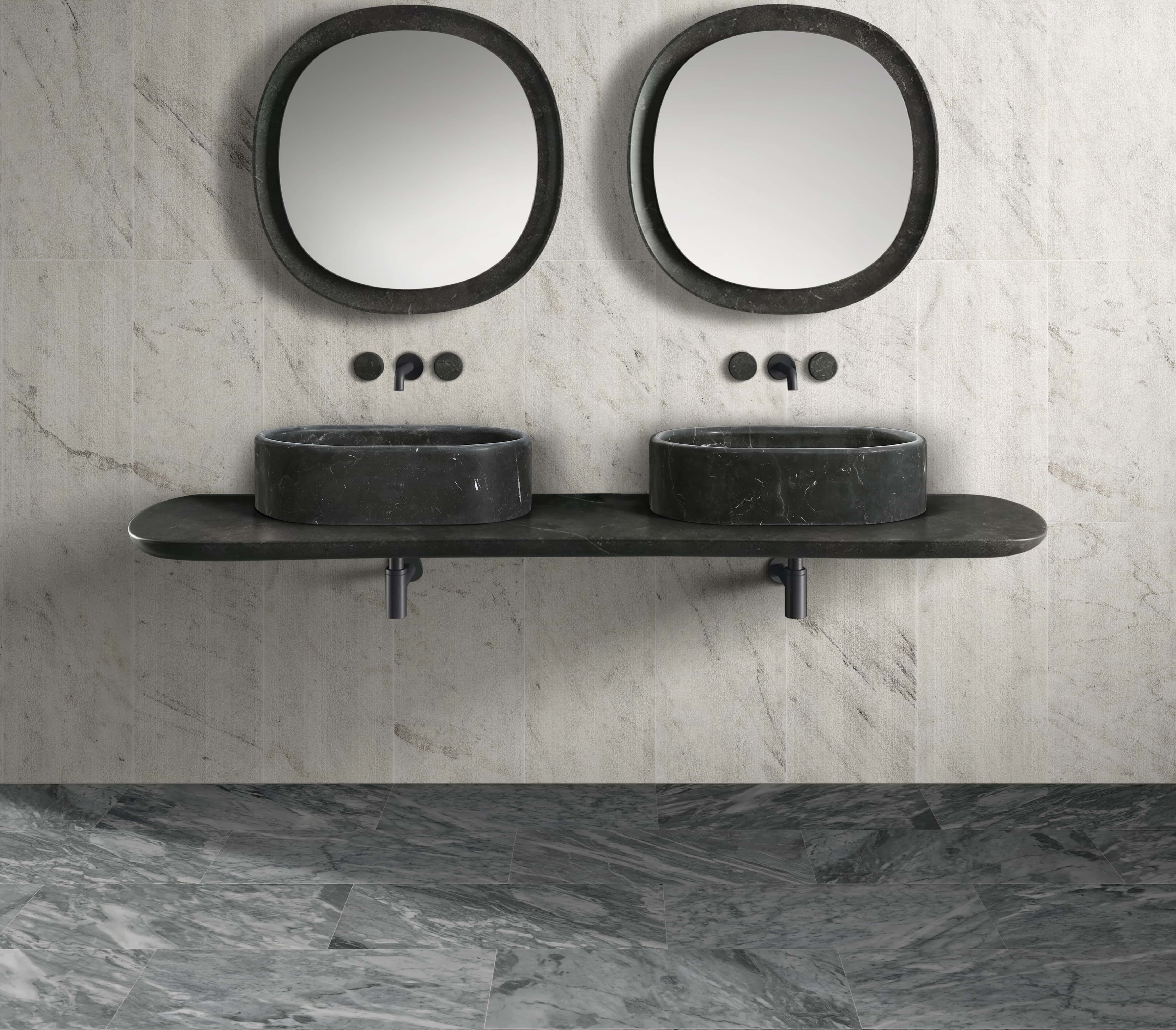 Two Olive Black marble oval vessel sinks paired with textured Snow Mountain White wall tile and polished Carrara gray floor tile.
