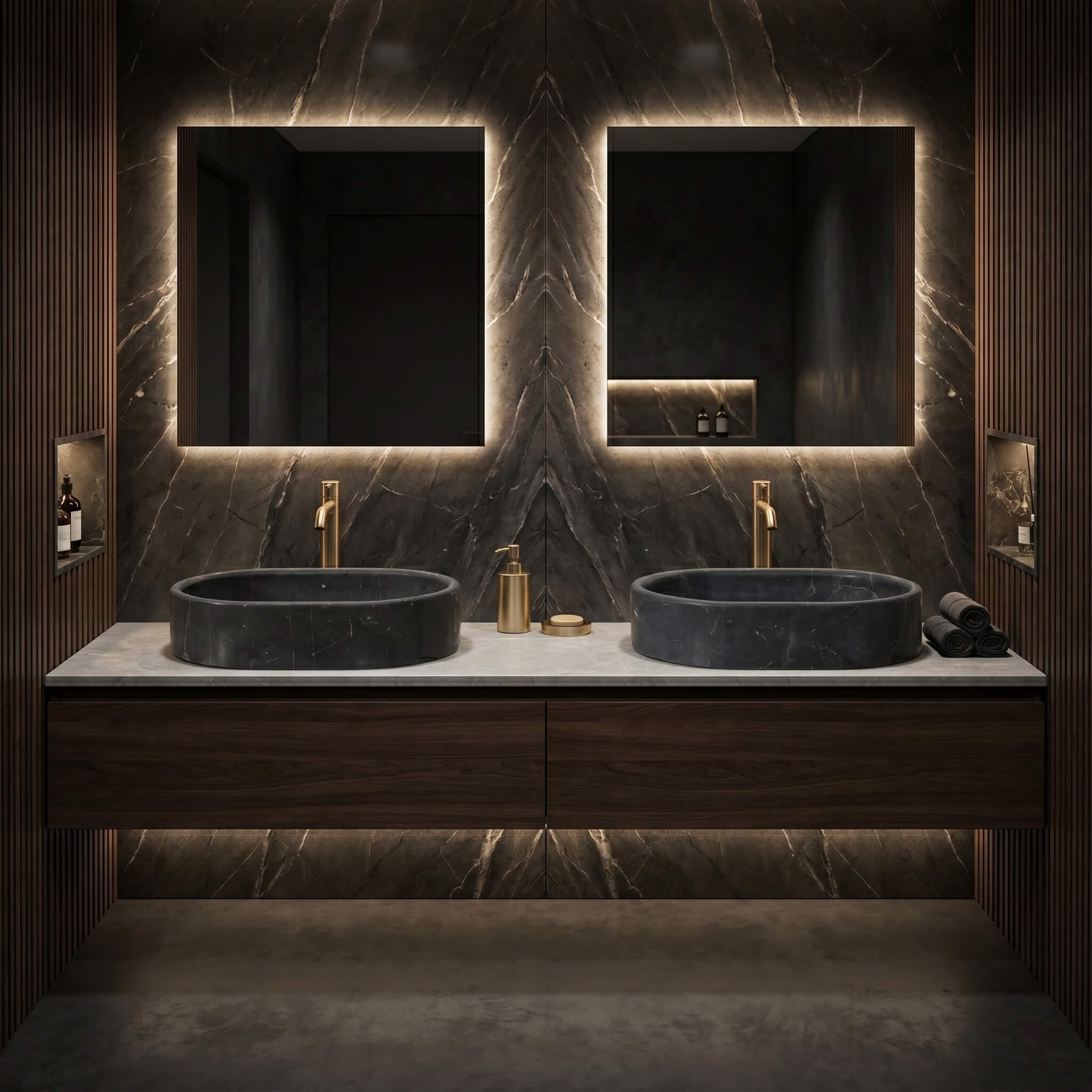 Two Olive Black marble oval vessel sinks on a light stone counter in a moody dark bathroom with walnut vanity and brass taps.