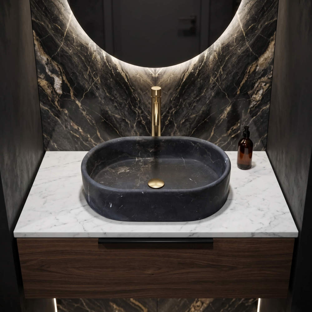 An Olive Black marble oval vessel sink on a walnut vanity below a backlit mirror, set against a dramatic veined stone wall.