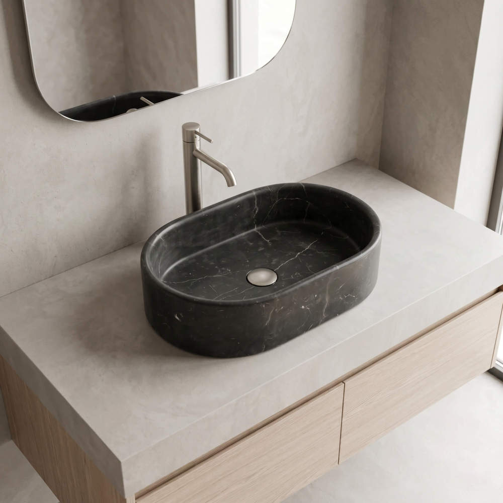 An Olive Black marble oval vessel sink on a light wood vanity with a brushed nickel tall faucet in a minimalist beige bathroom.