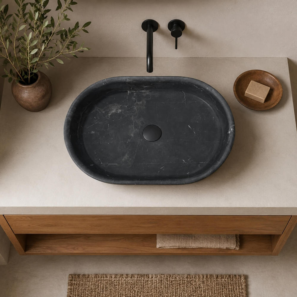 Overhead view of an Olive Black marble oval vessel sink on an oak vanity with cream counter and black wall-mounted taps.