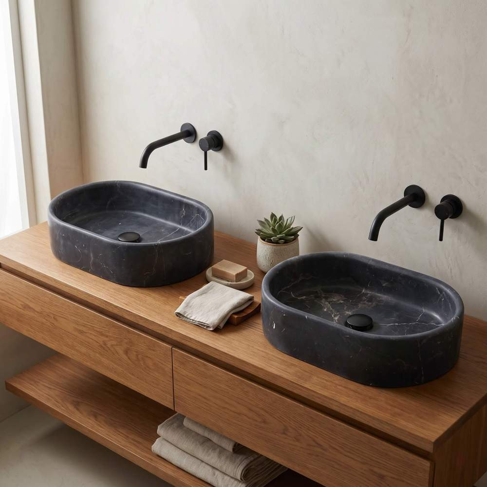 Two Olive Black marble oval vessel sinks on an oak vanity in a warm minimalist bathroom with microcement walls and black taps.