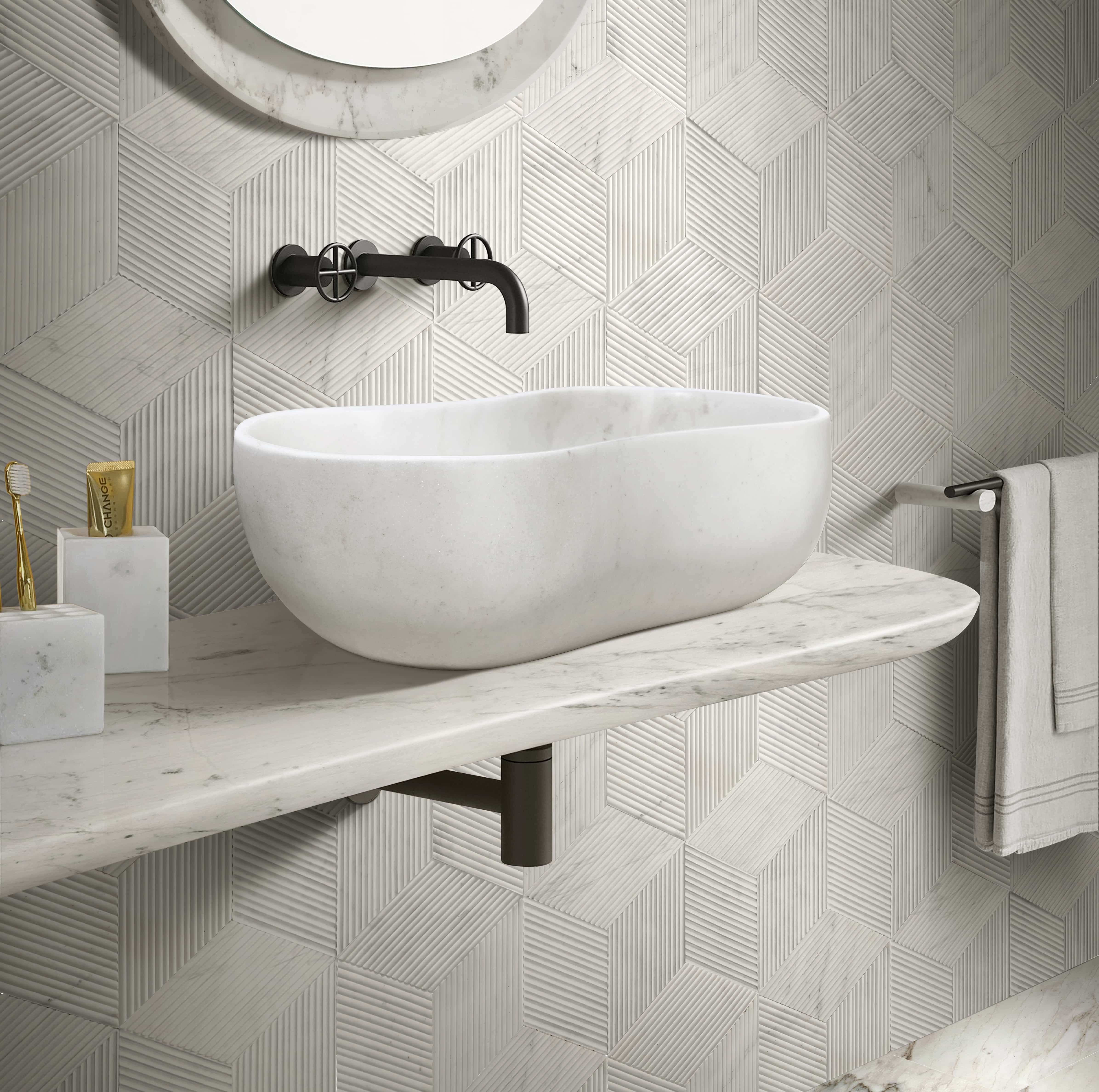 Single Snow Mountain White honed wavy marble vessel sink on a floating stone shelf against a wall lined with hexagon OL textured finished tiles, matching two pieces of marble bathroom accessories.