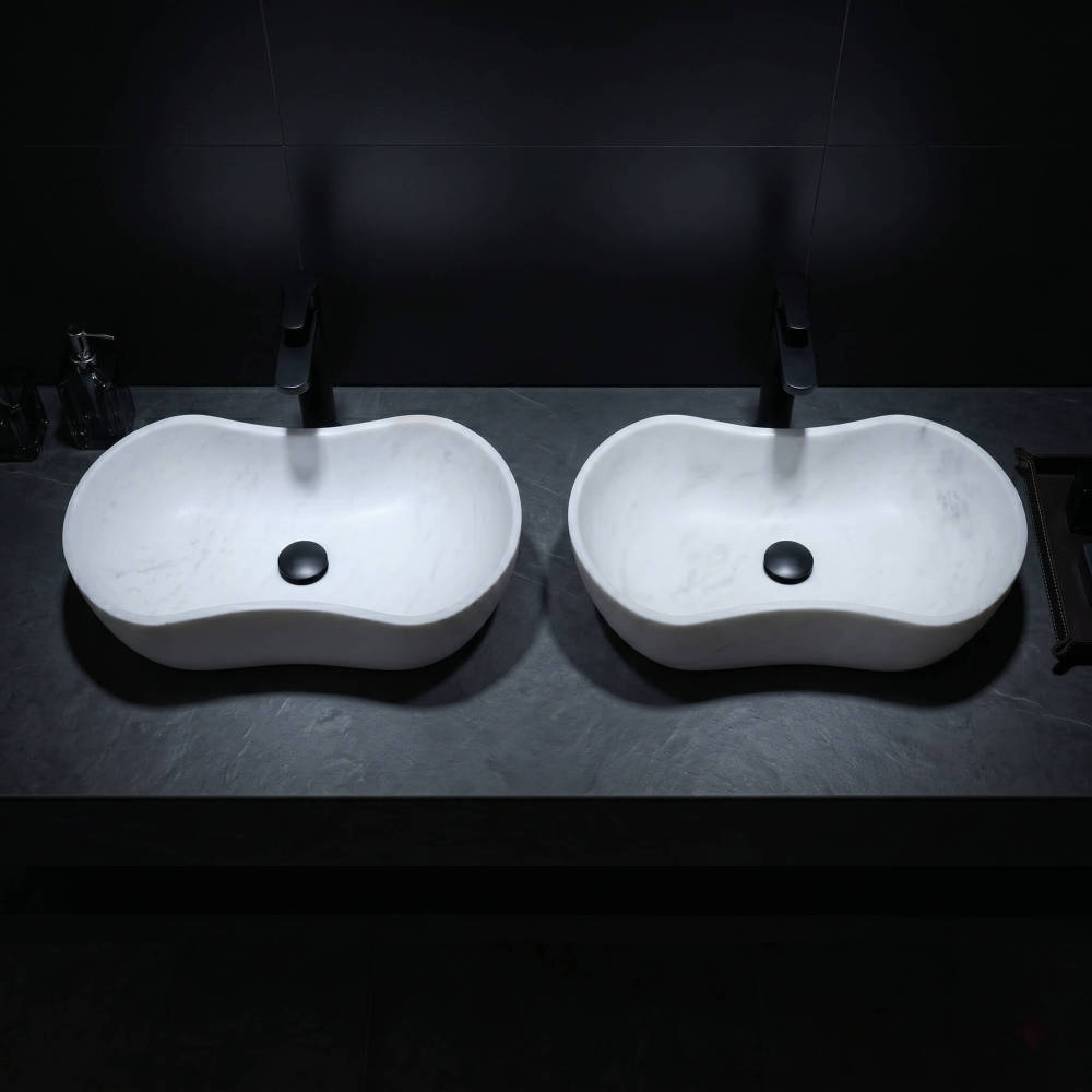 Top-down oblique shot of twin Snow Mountain White wavy marble basins on a textured dark charcoal slate countertop with matte black fixtures under dramatic minimalist spotlighting.