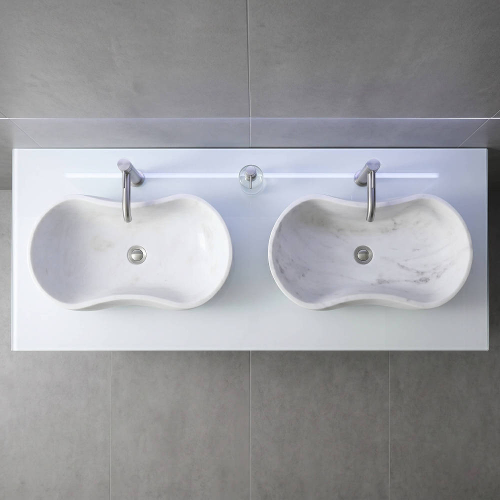 Direct overhead view of two natural marble wavy vessel sinks on a sleek translucent white backlit counter surrounded by seamless large-format matte grey concrete wall and floor tiles.