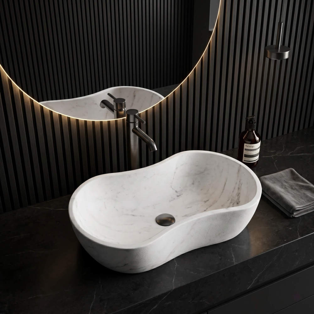 High-angle 3/4 view of the wavy marble vessel sink on a black marble counter. Features a sleek dark faucet and drain against a dark vertical slat wall. A large circular backlit LED mirror is visible. Modern sleek design.