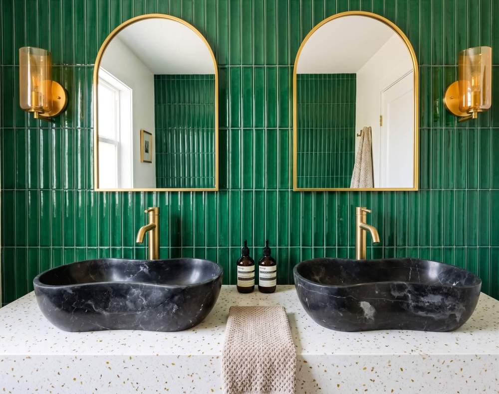 A vibrant luxury bathroom design featuring dual Olive Black natural marble wave sinks on a terrazzo countertop against an emerald green tiled wall.