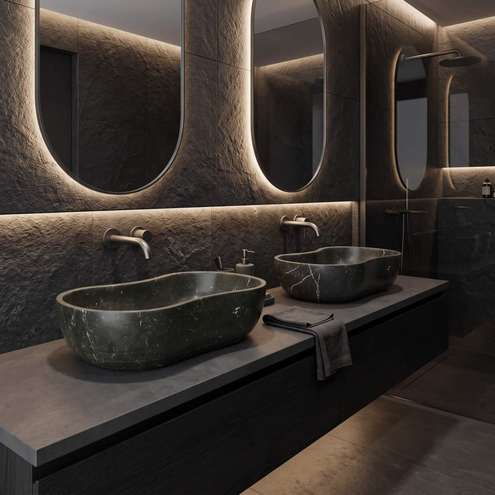 A modern minimalist bathroom design utilizing a moody charcoal palette, with backlit oval mirrors highlighting two Olive Black marble wave sinks.