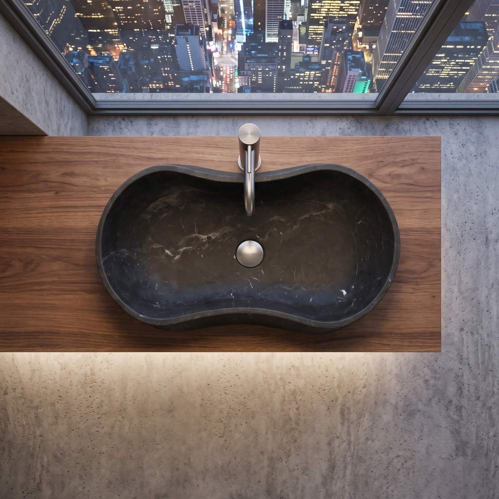Top-down view of a honed Olive Black natural marble wave sink installed on a rich wood grain vanity in a luxury urban high-rise apartment.