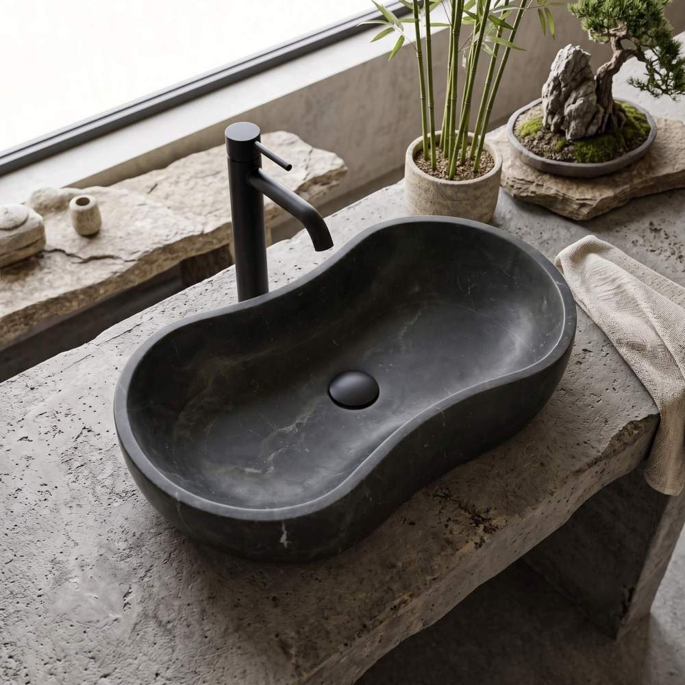 A honed Olive Black natural marble wave vessel sink paired with a matte black faucet on a textured concrete countertop in a zen-inspired bathroom.