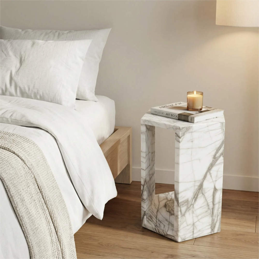 Arboris White natural marble hexagon pedestal nightstand styled with a candle and art book beside a cozy bed.