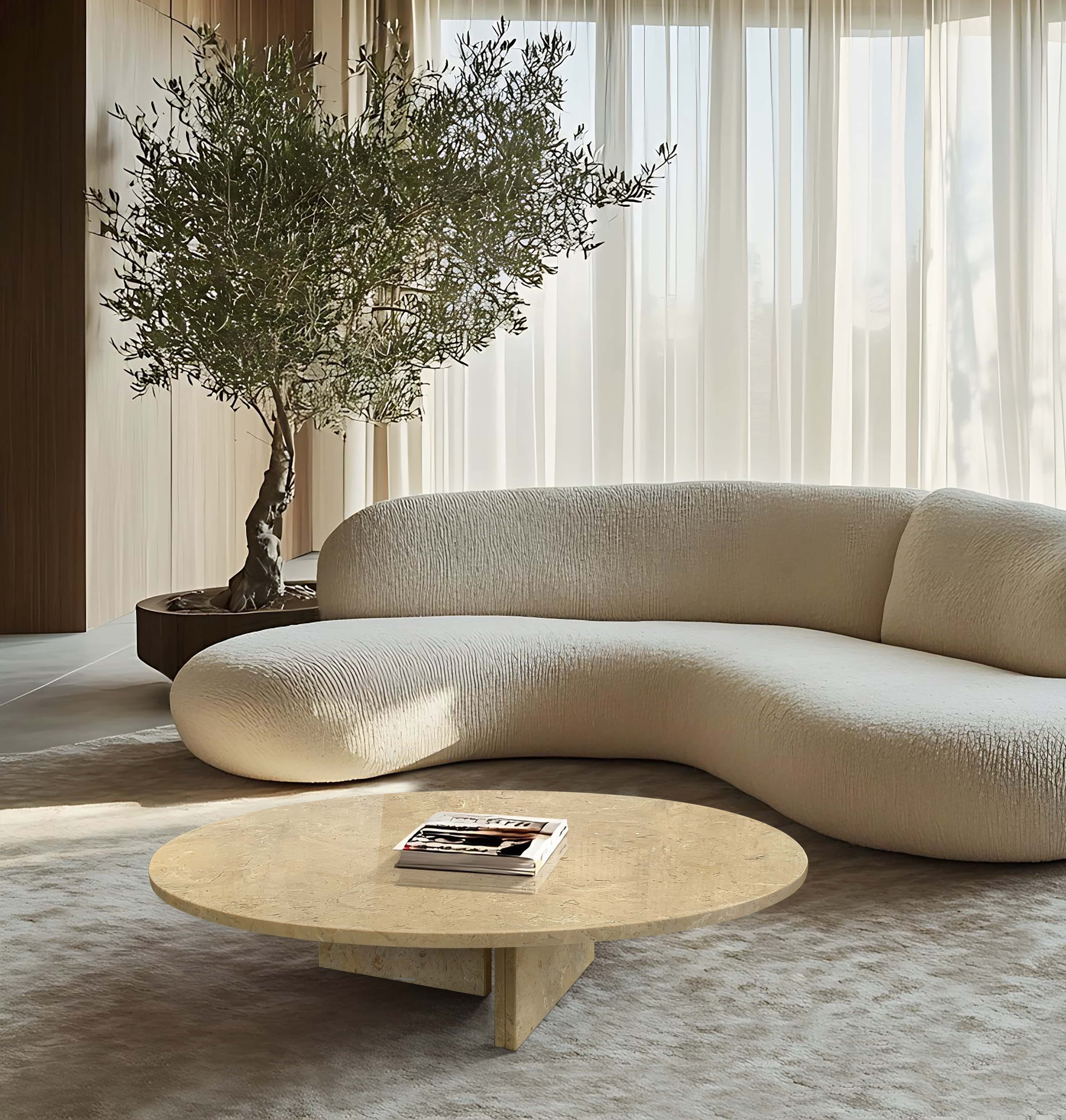 Round Amber Gold marble coffee table grounding a curved textured sofa and olive tree in a Mediterranean minimalist living room.