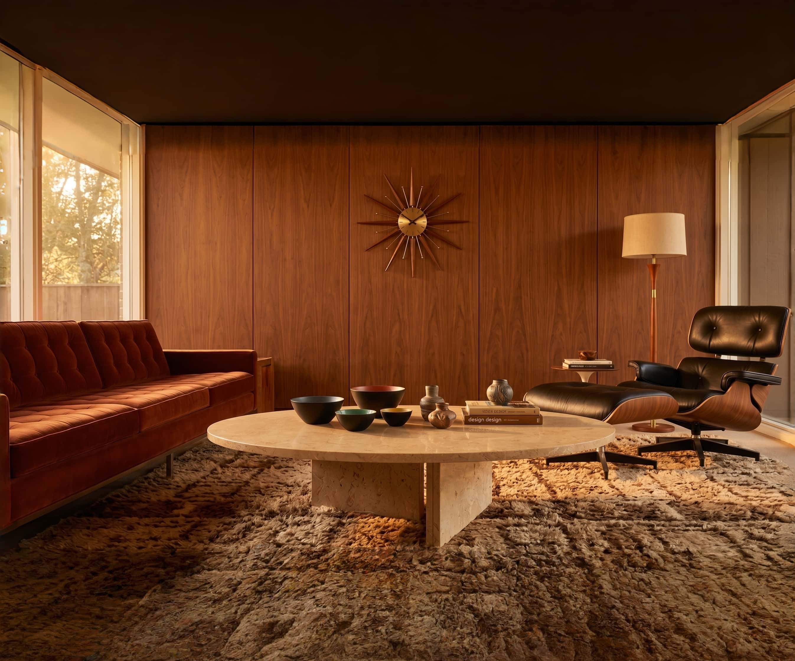 Round Amber Gold marble coffee table with rust velvet sofa and Eames lounge chair in a mid-century walnut-paneled den.