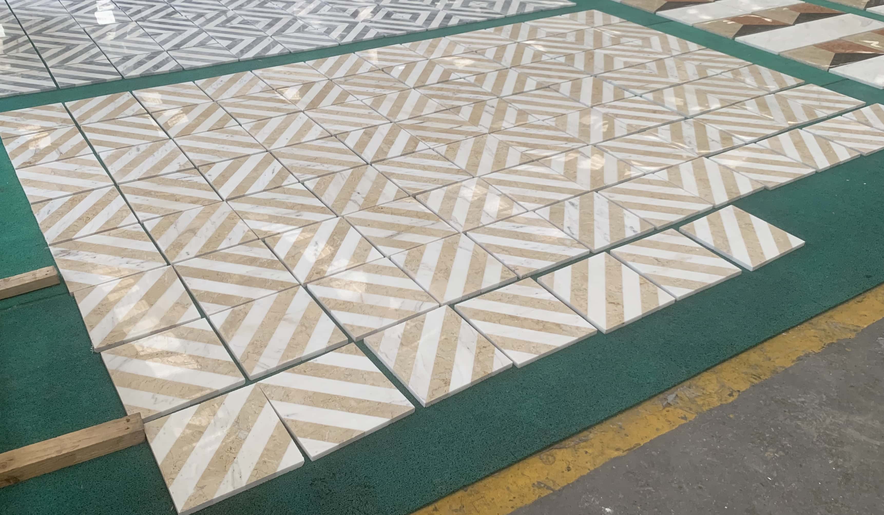 White and gold diagonal stripe waterjet marble tiles laid out on factory floor in a repeated chevron pattern.