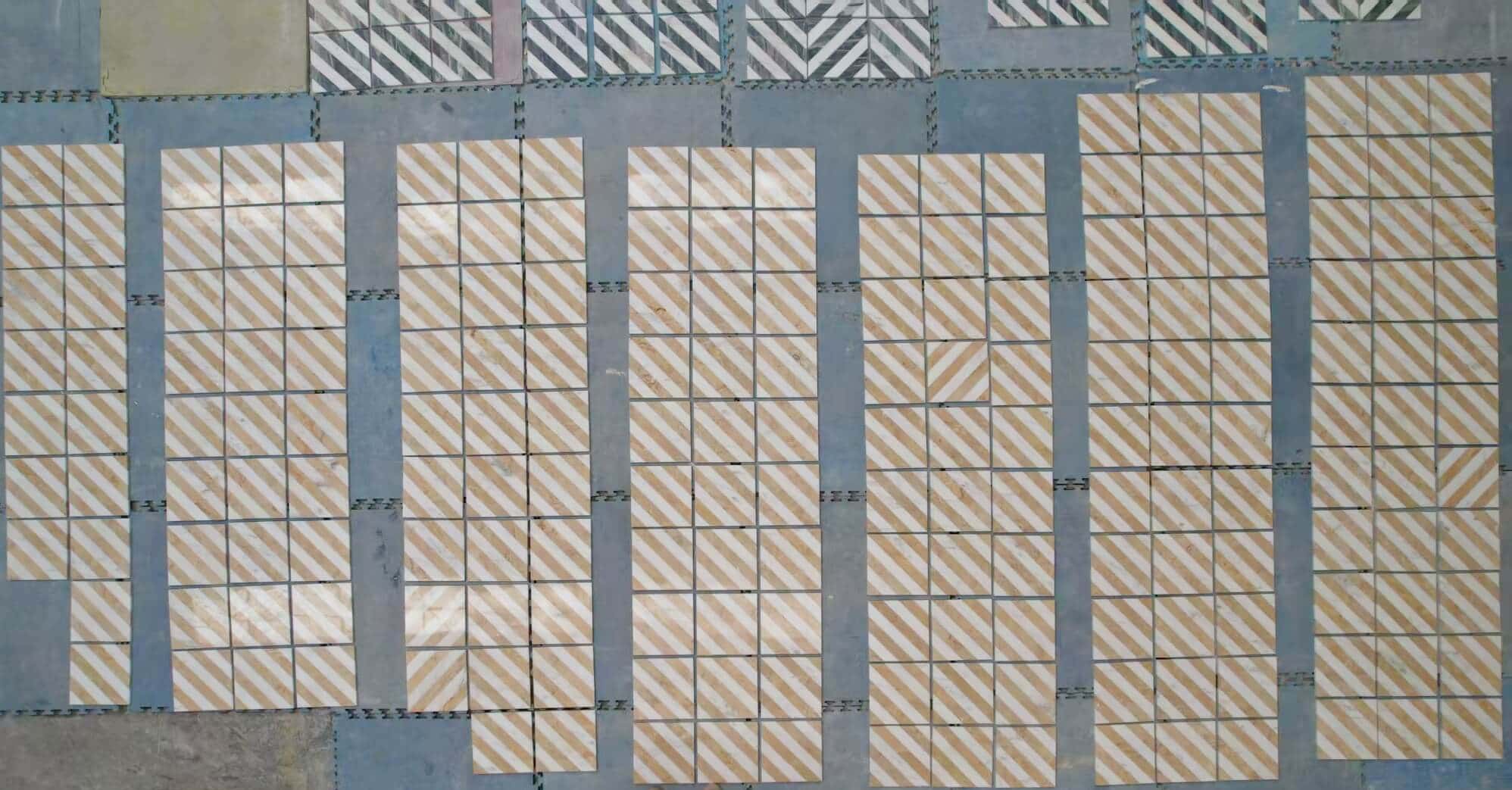 Factory floor dry layout of white and gold diagonal stripe marble tiles displaying natural stone veining variations.