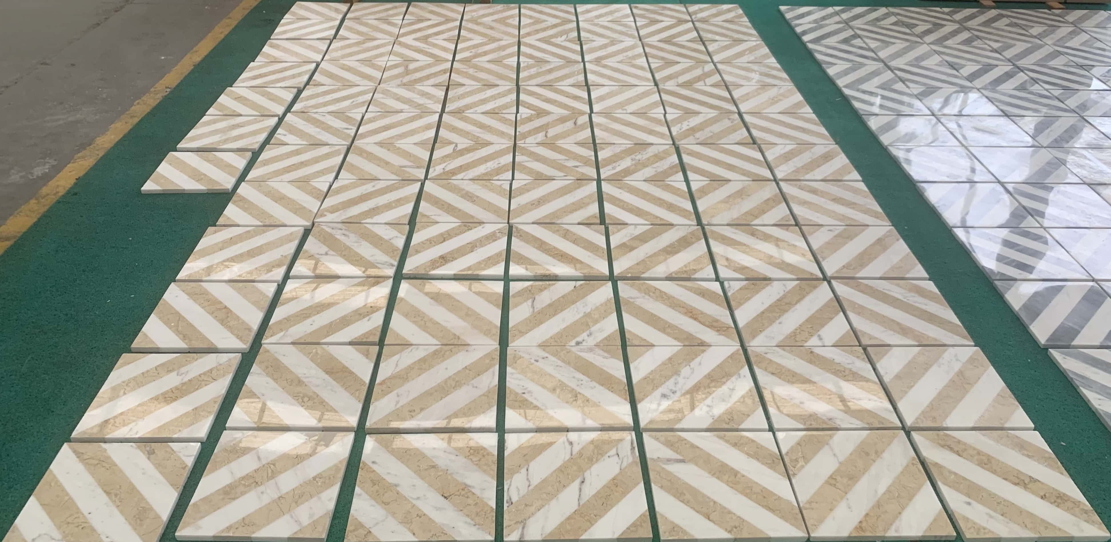 Perspective view of polished white and gold waterjet marble tiles on factory floor reflecting overhead lighting.
