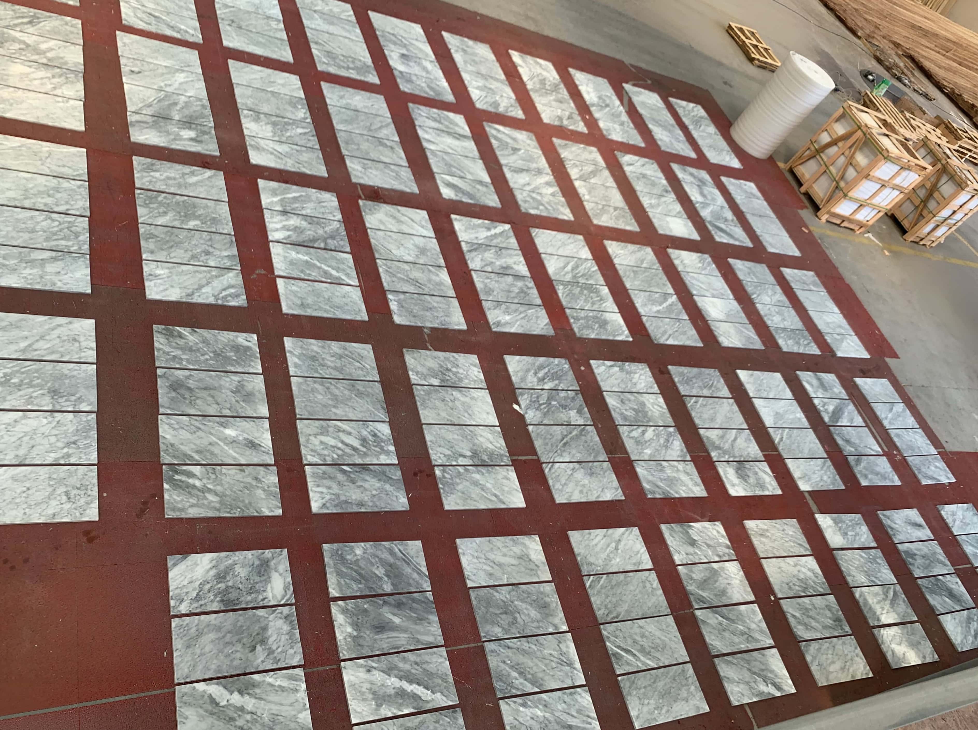 Factory staging floor with 12x24 Carrara Gray polished marble tile batches arranged near wooden export crates for packing.