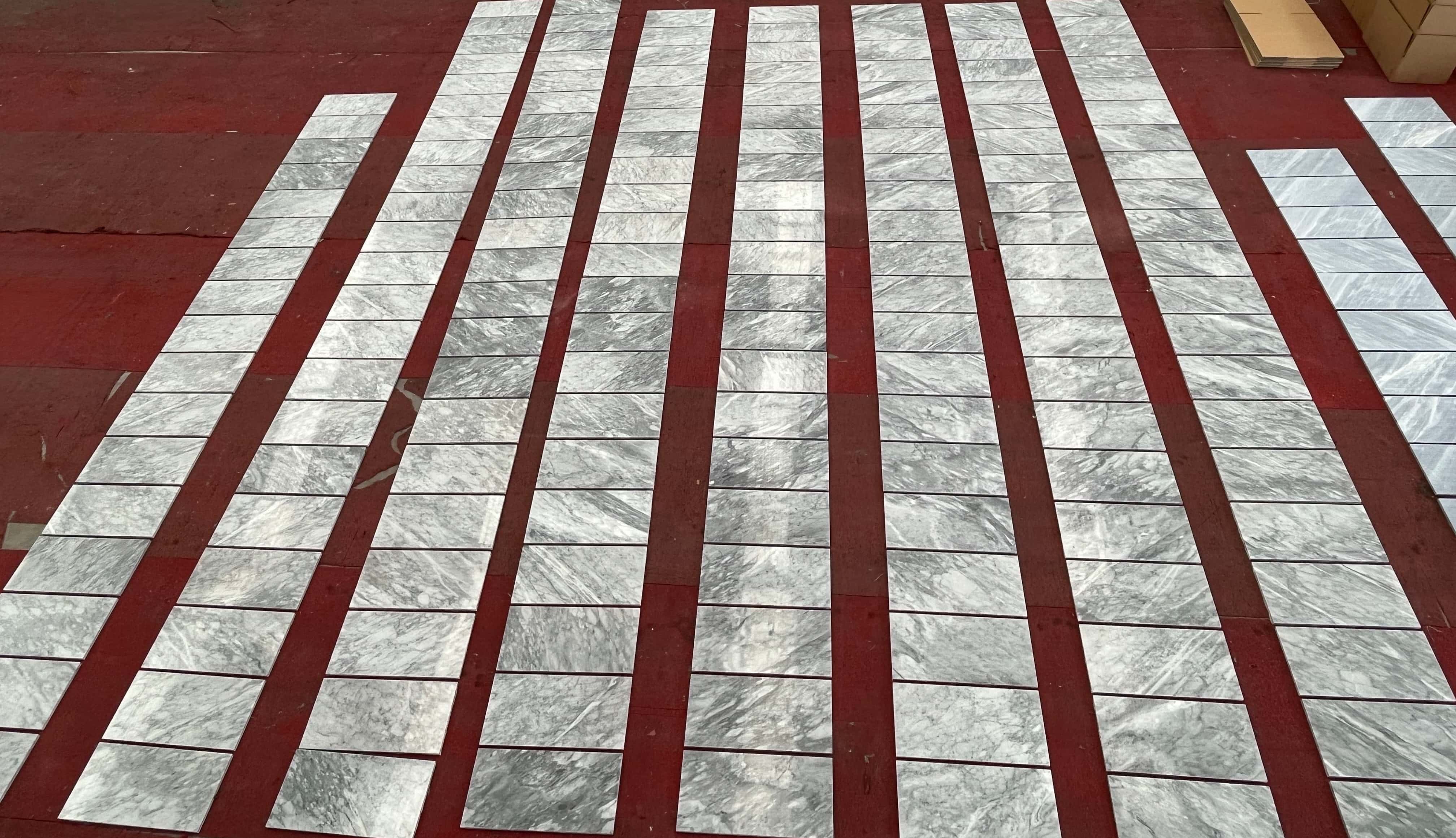 Factory quality control inspection of 12x24 Carrara Gray polished marble tiles laid out in rows for color shade matching.