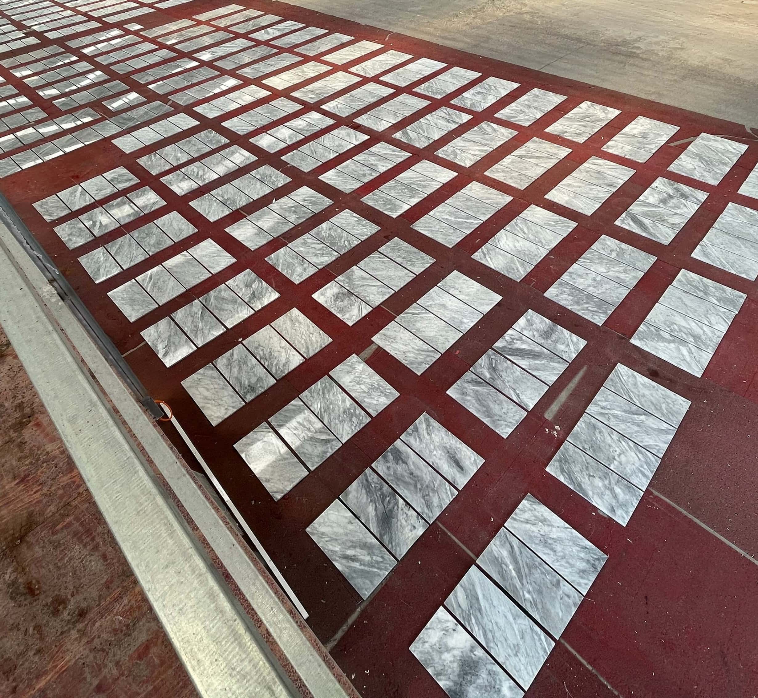 High angle factory view of 12x24 Carrara Gray polished marble tiles laid out for final quality control before packing.