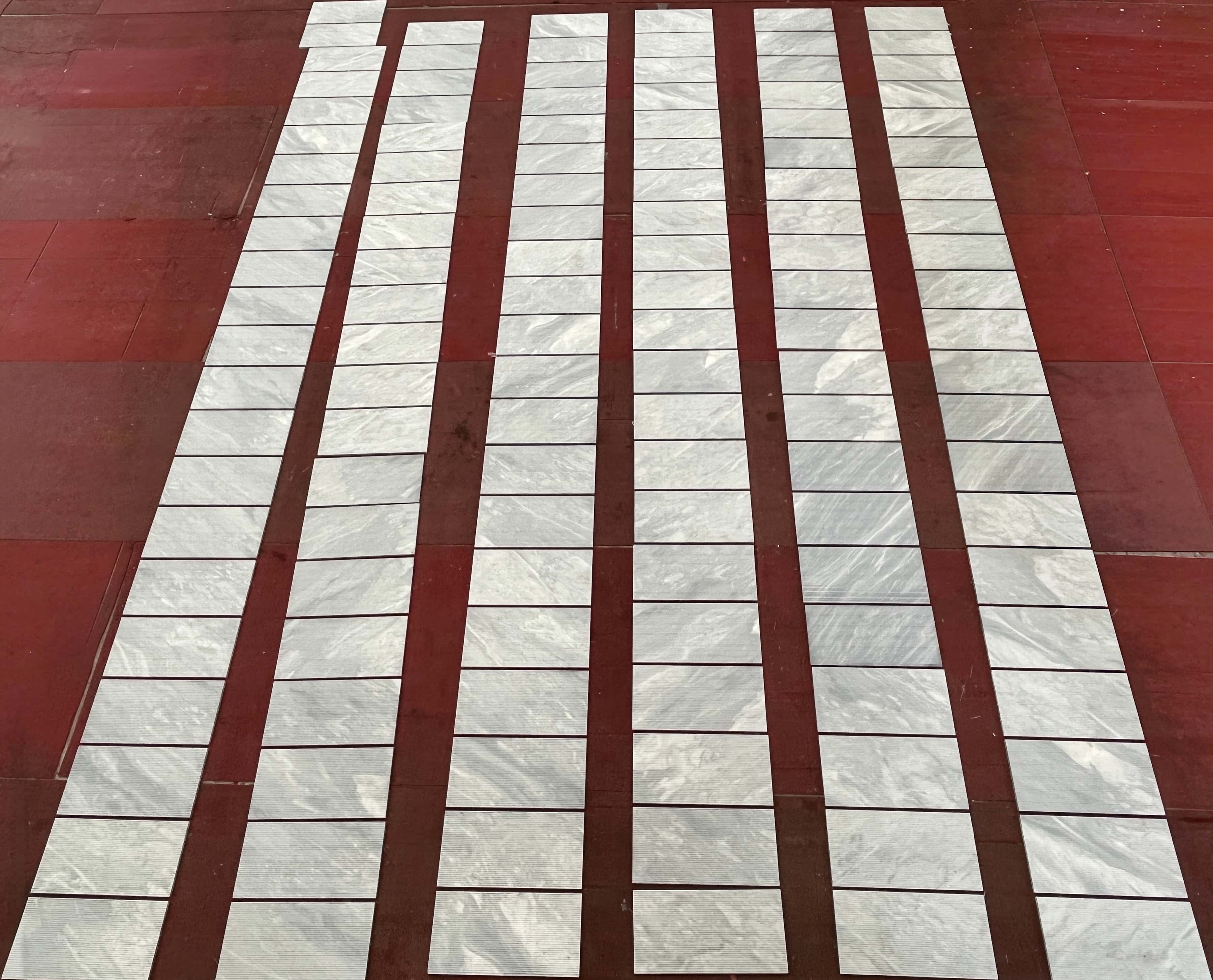 High-angle view of multiple fluted marble tiles laid out in long rows on a floor, highlighting natural variation.