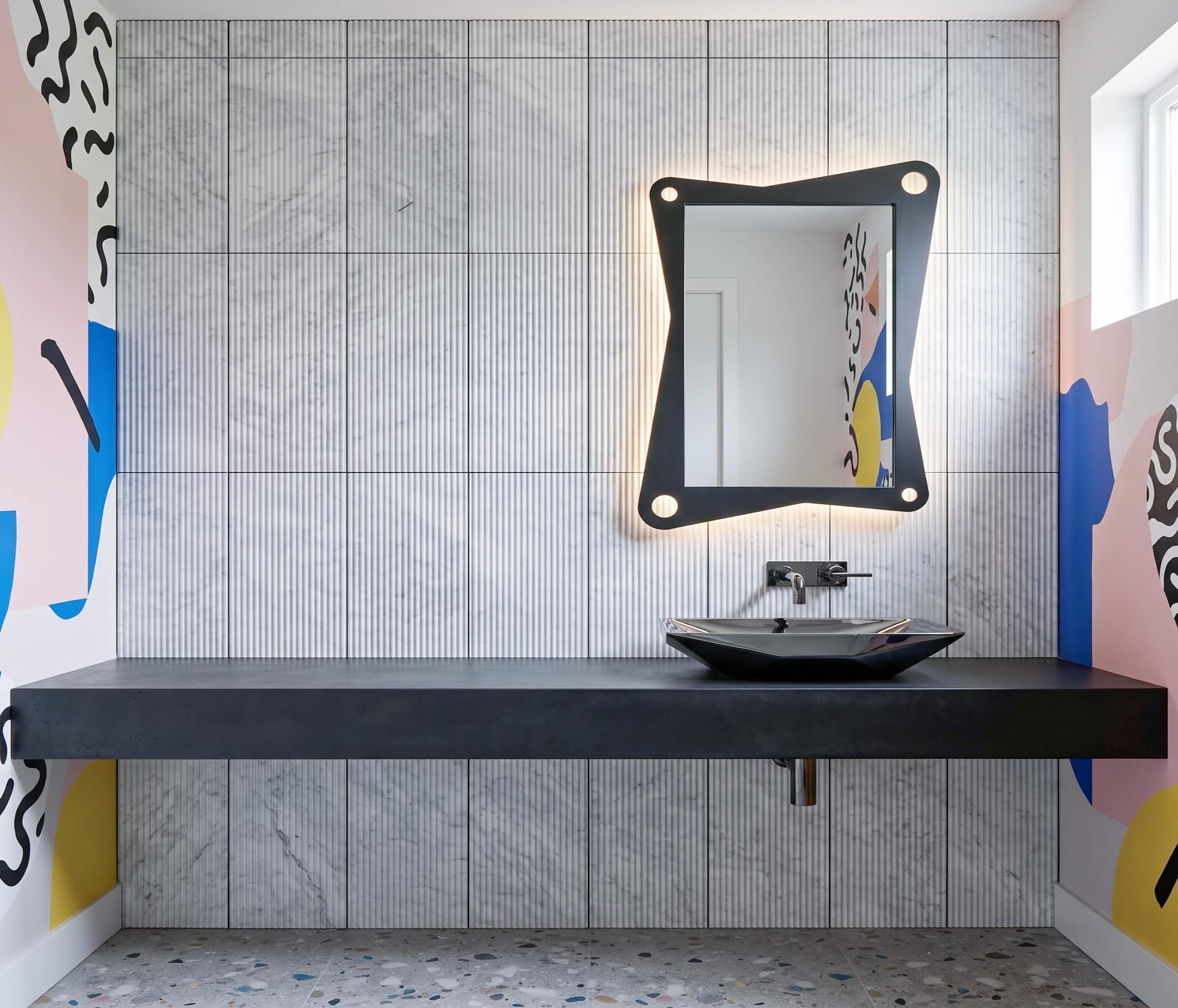 Black bathroom vanity with vessel sink set against a 12x24 fluted Carrara gray marble tile feature wall.