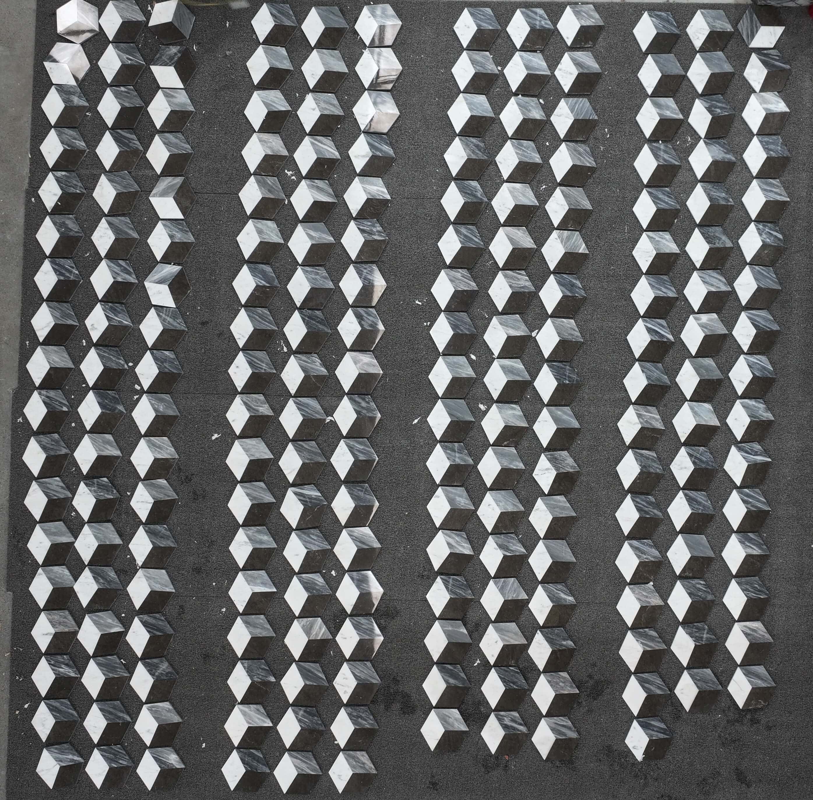 Factory quality check displaying organized rows of white, gray, and black 3D cube natural marble tiles before shipping.