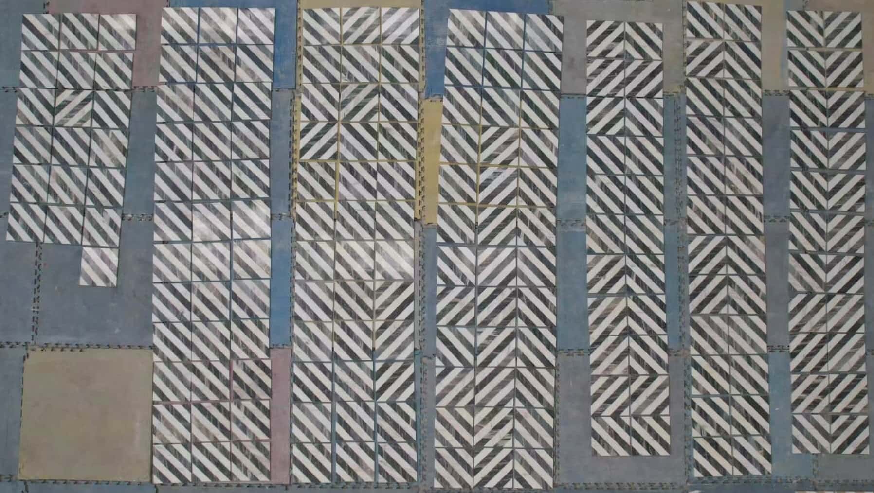 Factory quality dry-lay inspection showing white and gray waterjet marble tiles arranged in continuous chevron patterns.