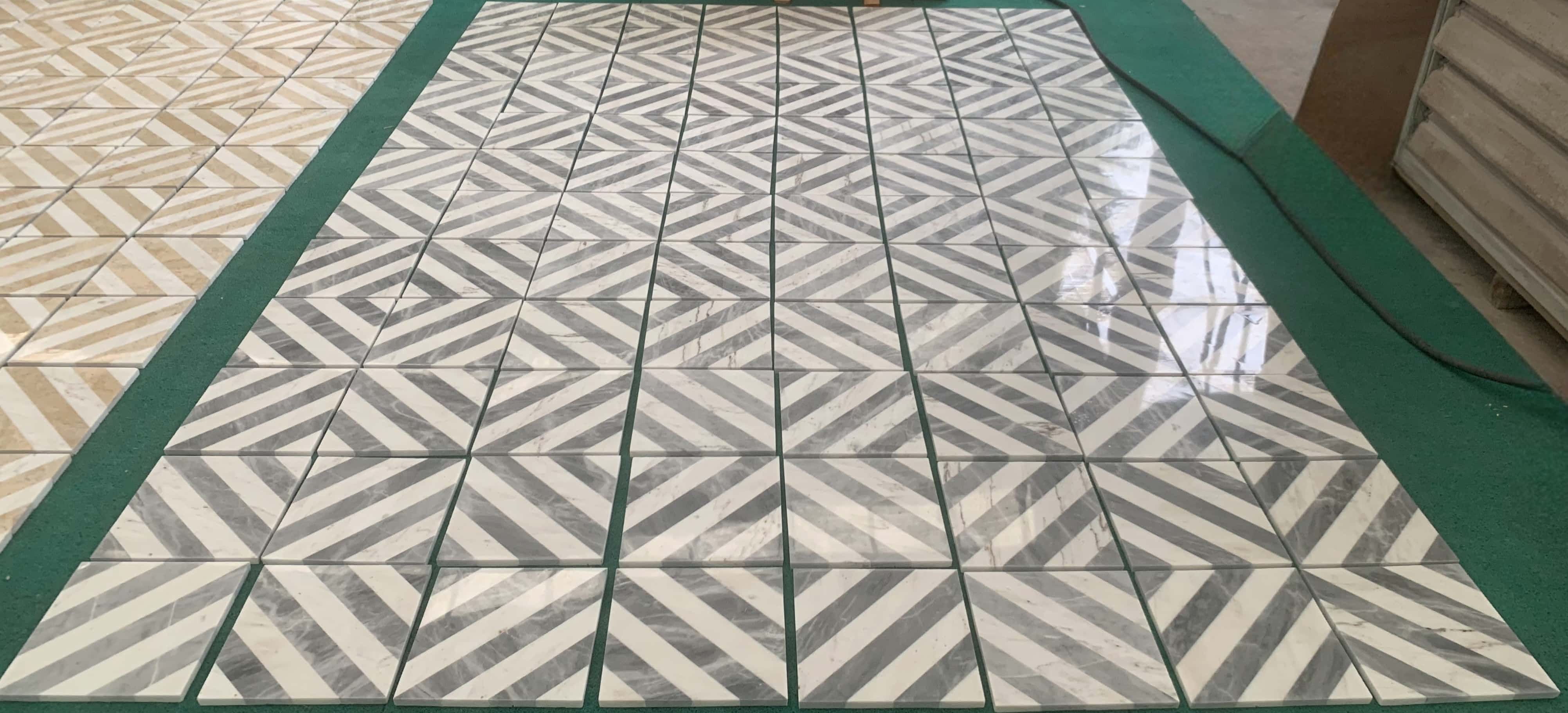 High-gloss polished surface of white and gray waterjet marble tiles reflecting ambient light on factory layout mat.