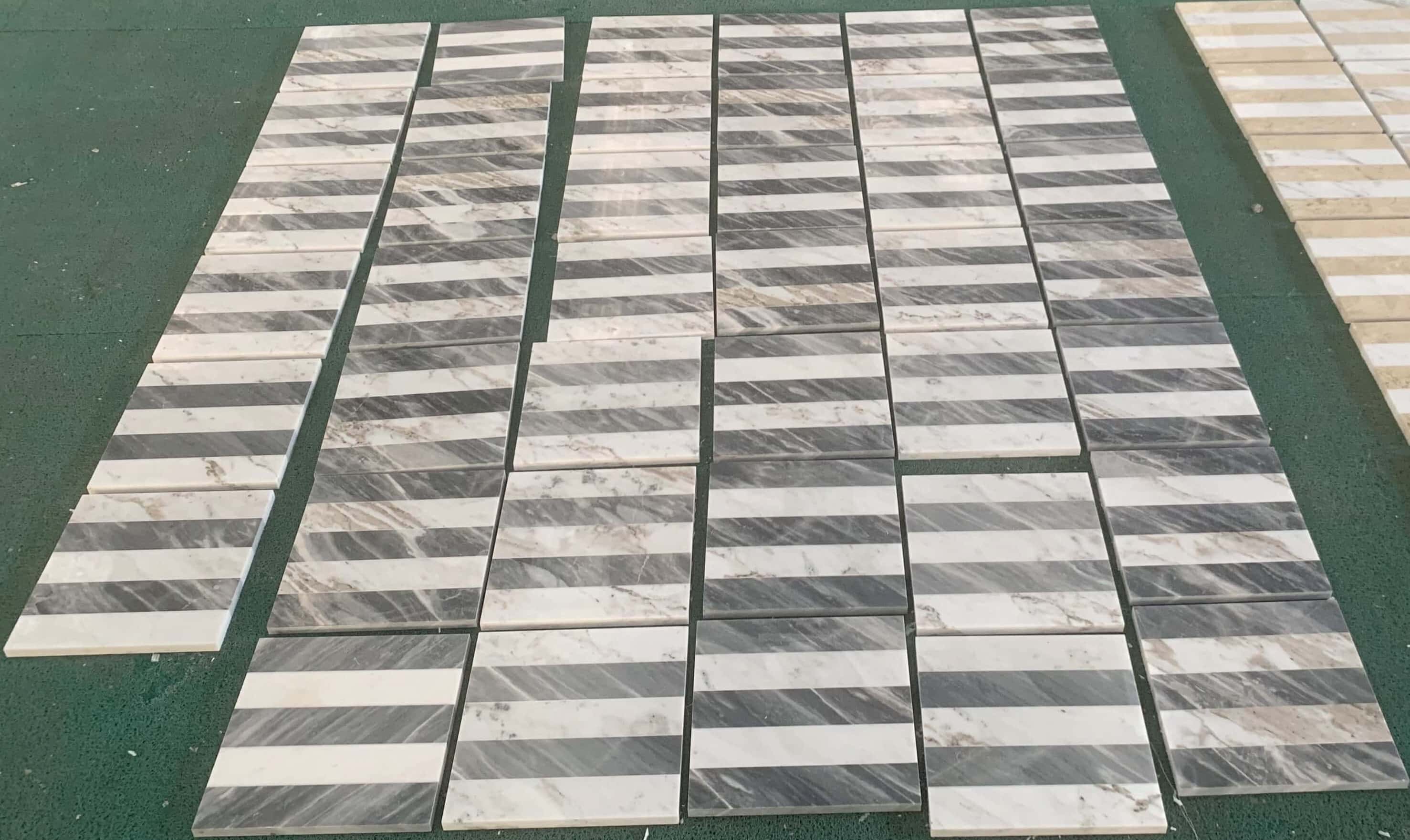 Factory quality inspection setup on green floor mat displaying aligned Snow Mountain White and Carrara Gray waterjet tiles.