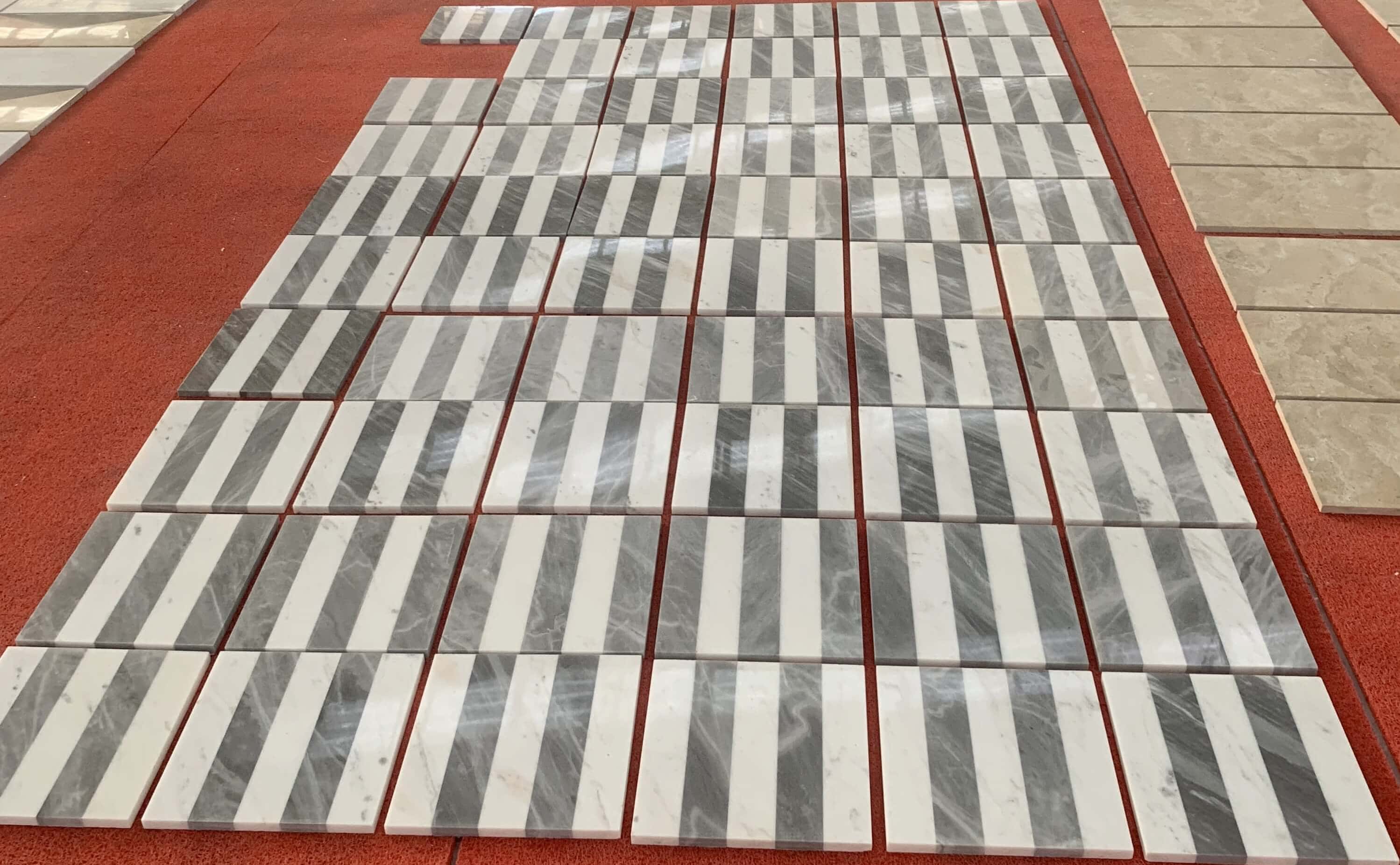 Factory perspective display of polished Snow Mountain White and Carrara Gray waterjet marble tiles on red inspection floor.