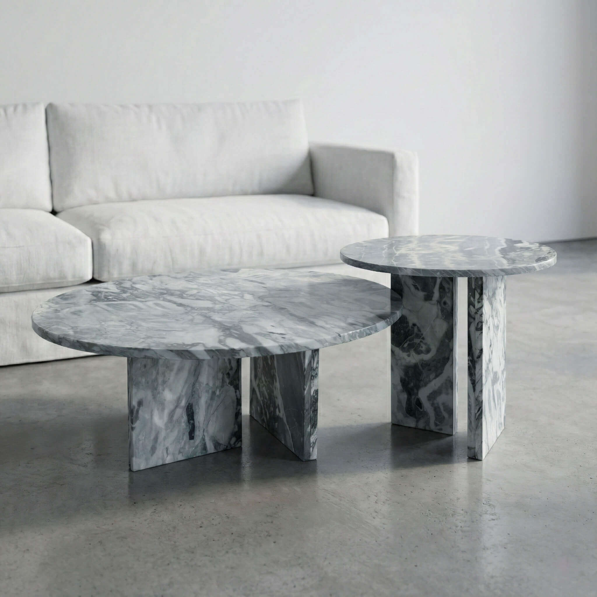 Modern cloudy blue marble tables with round polished tops and solid upright bases set against a minimal white sofa and floor.