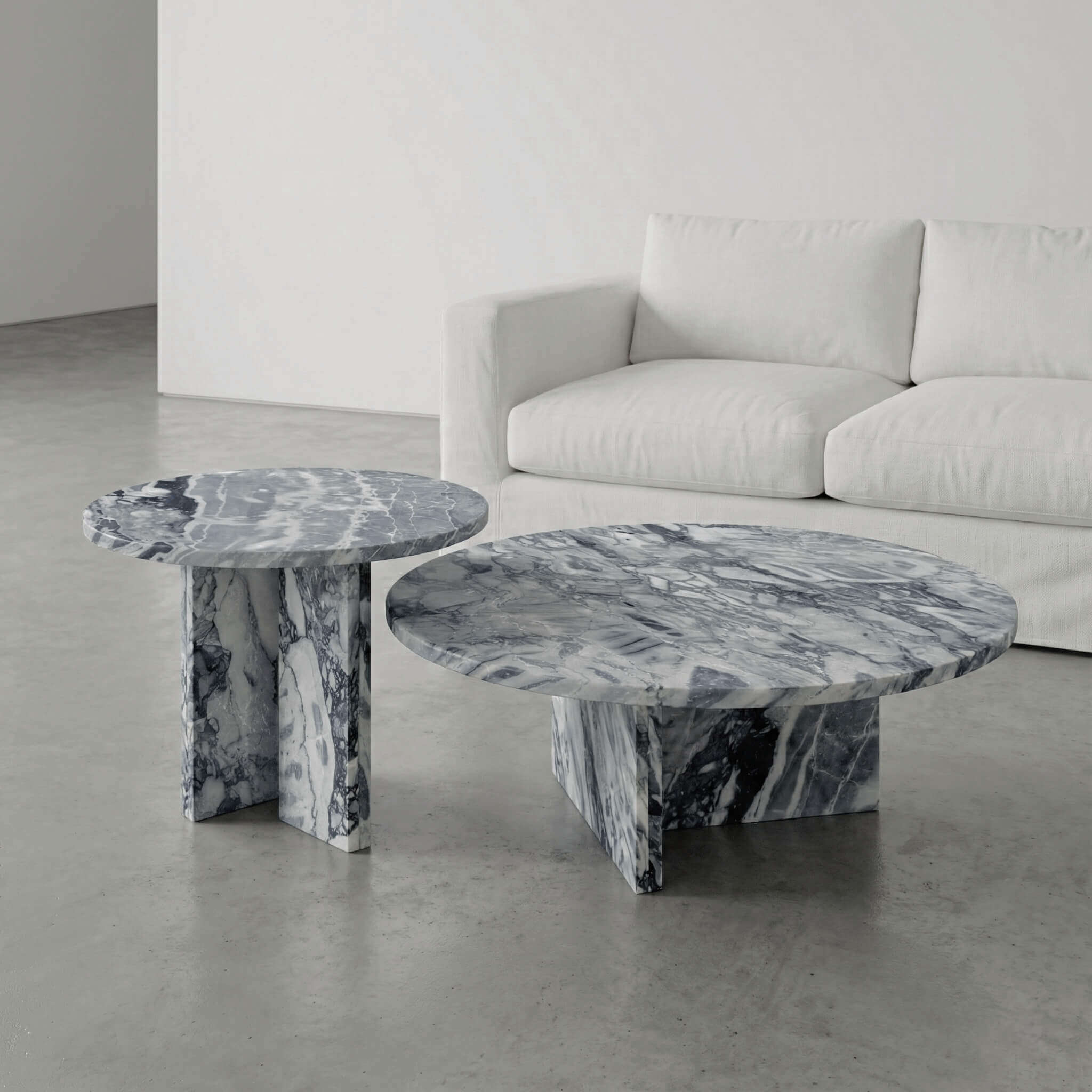 Set of two round marble coffee tables in cloudy blue stone showcasing organic veining next to a modern white fabric sofa.