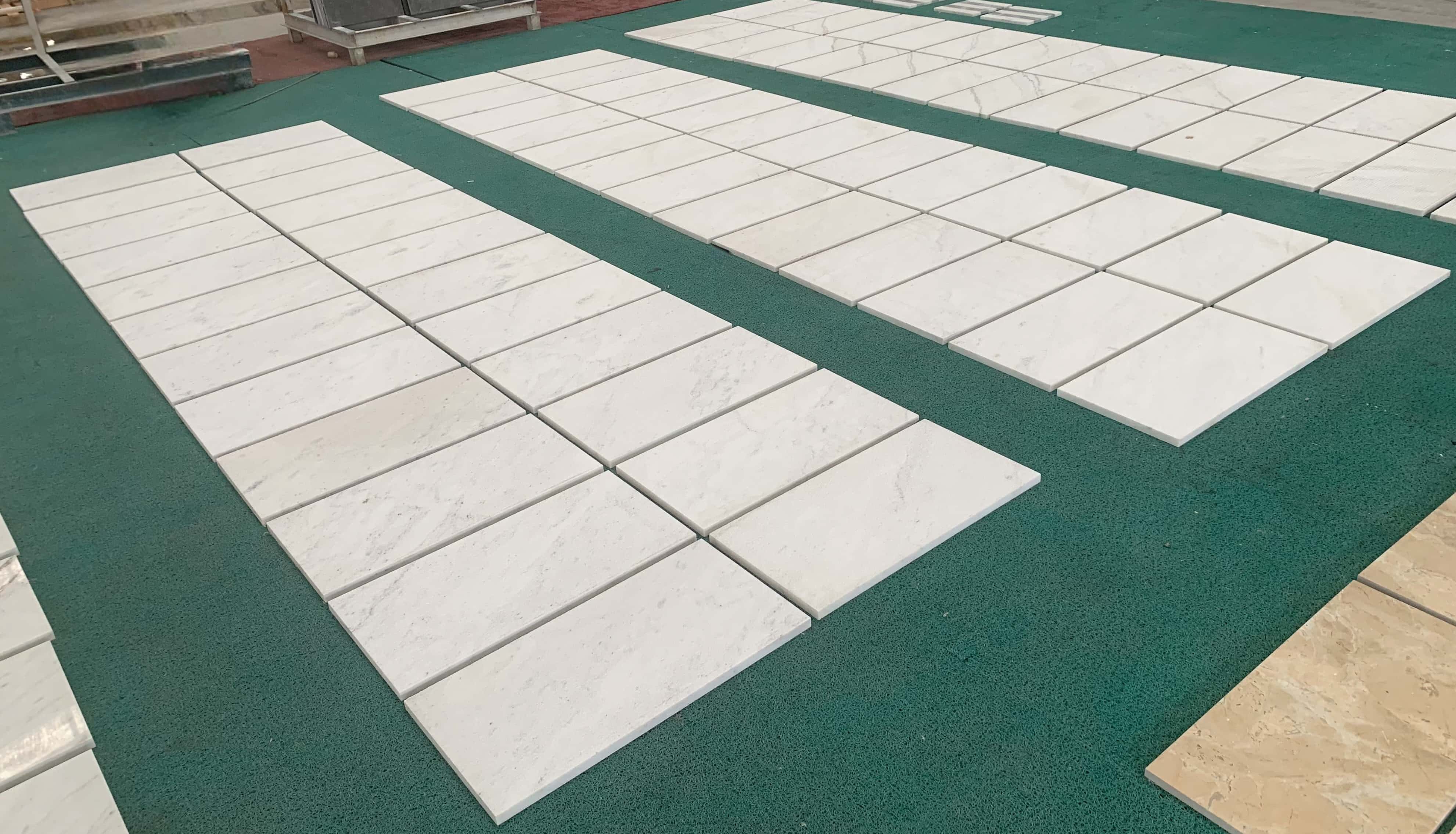 Factory quality check showing variation across multiple 12x24 Snow Mountain White FS textured marble tiles on dry-lay mats.