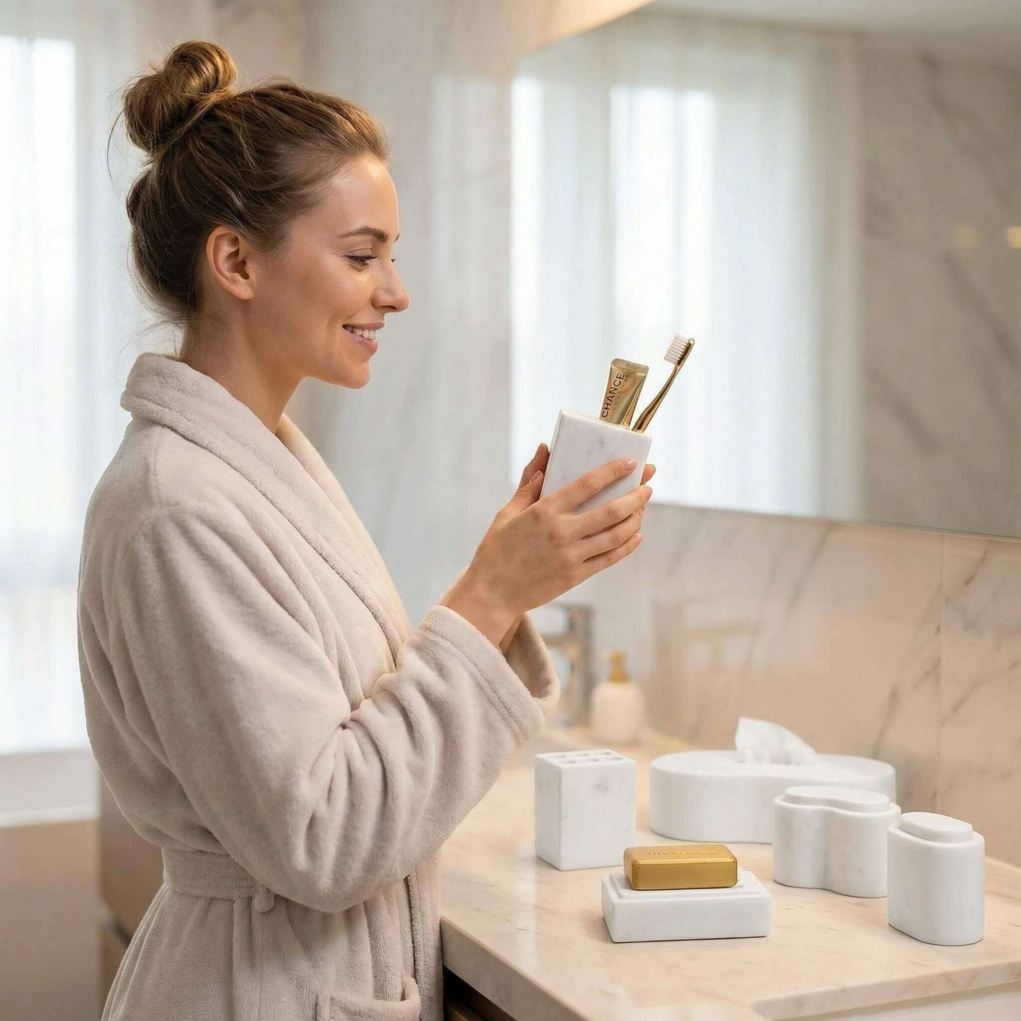 Woman holding the Snow Mountain White marble square toothpaste tube holder beside the 6-piece set on a vanity.