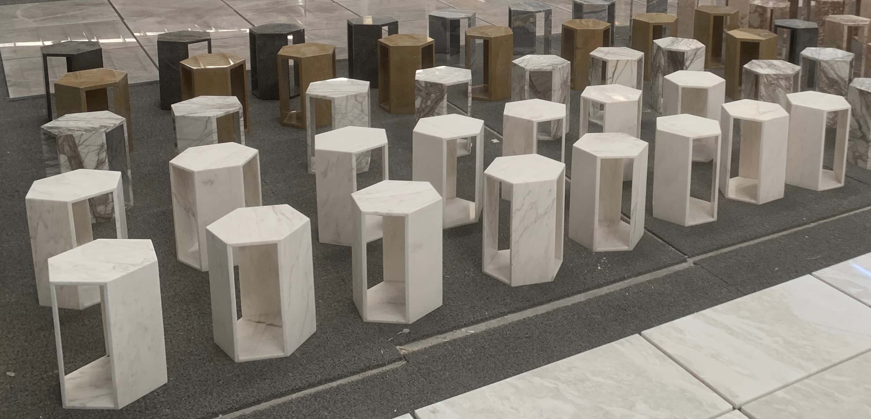 Factory production view showing multiple honed Snow Mountain White marble hexagon side tables during assembly.