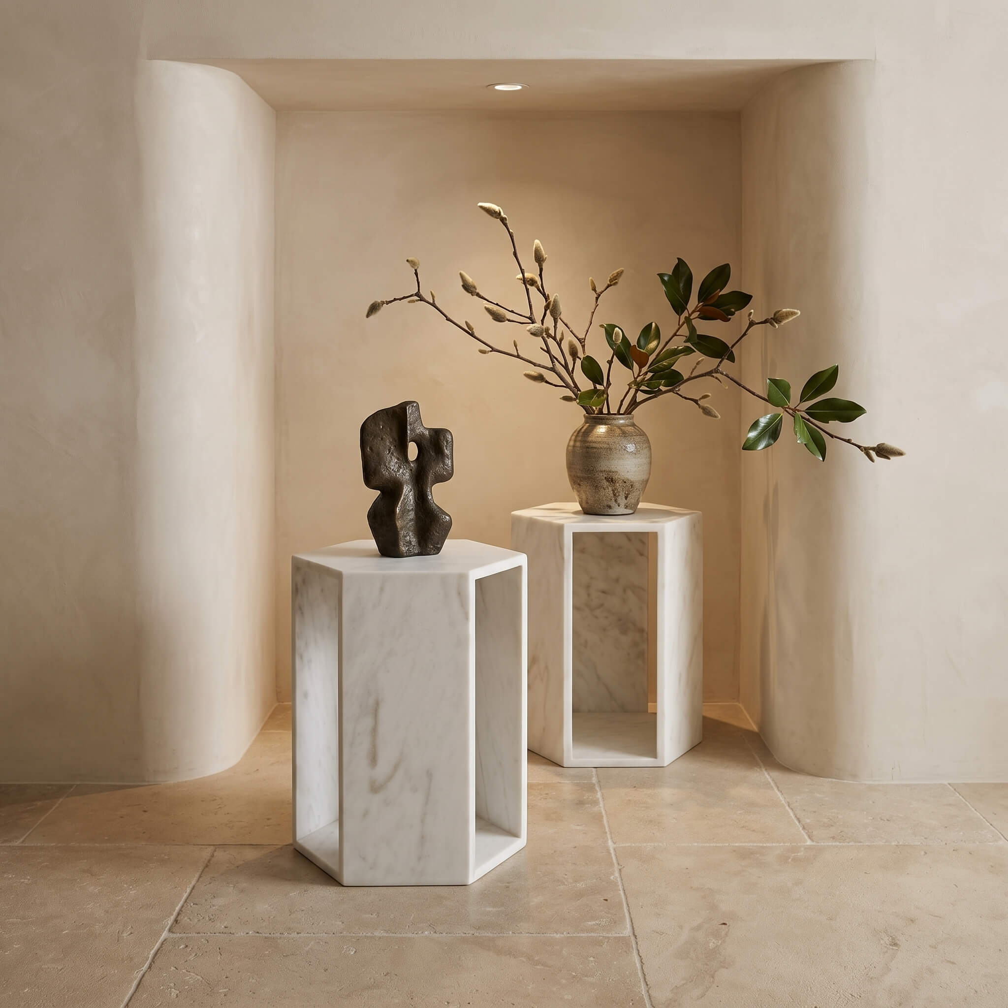 Honed Snow Mountain White marble hexagon tables used as elegant display pedestals for art and branches in a warm alcove.