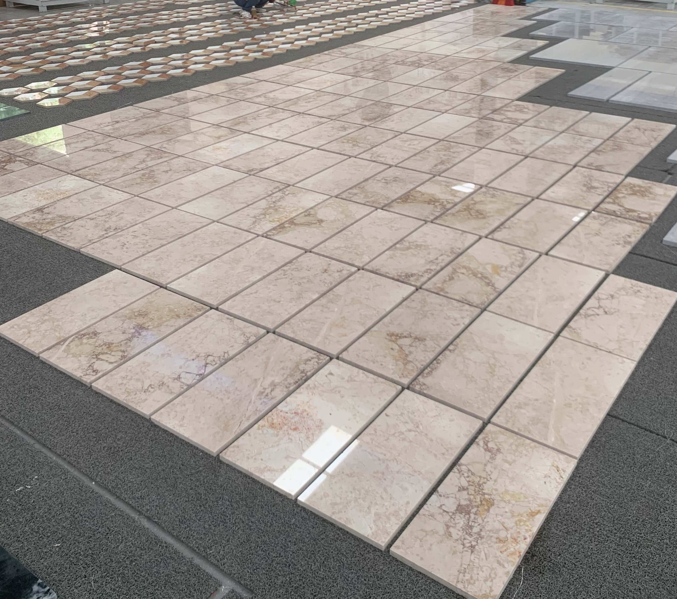Angled factory dry-lay of 12x24 Diamond Pink marble floor tile showcasing mirror-gloss polished breccia reflection.