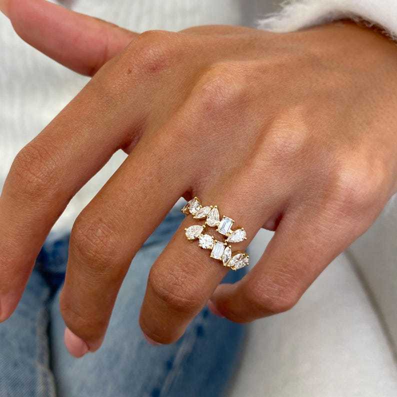 Top-down perspective of an open shank diamond ring on a hand, showing how the emerald and pear cut stones wrap around the finger for a floating effect.