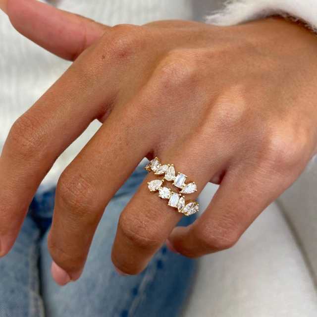 Top-down perspective of an open shank diamond ring on a hand, showing how the emerald and pear cut stones wrap around the finger for a floating effect.