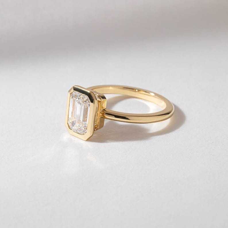 Sleek 14K gold band and full bezel setting securing an emerald cut lab created diamond.