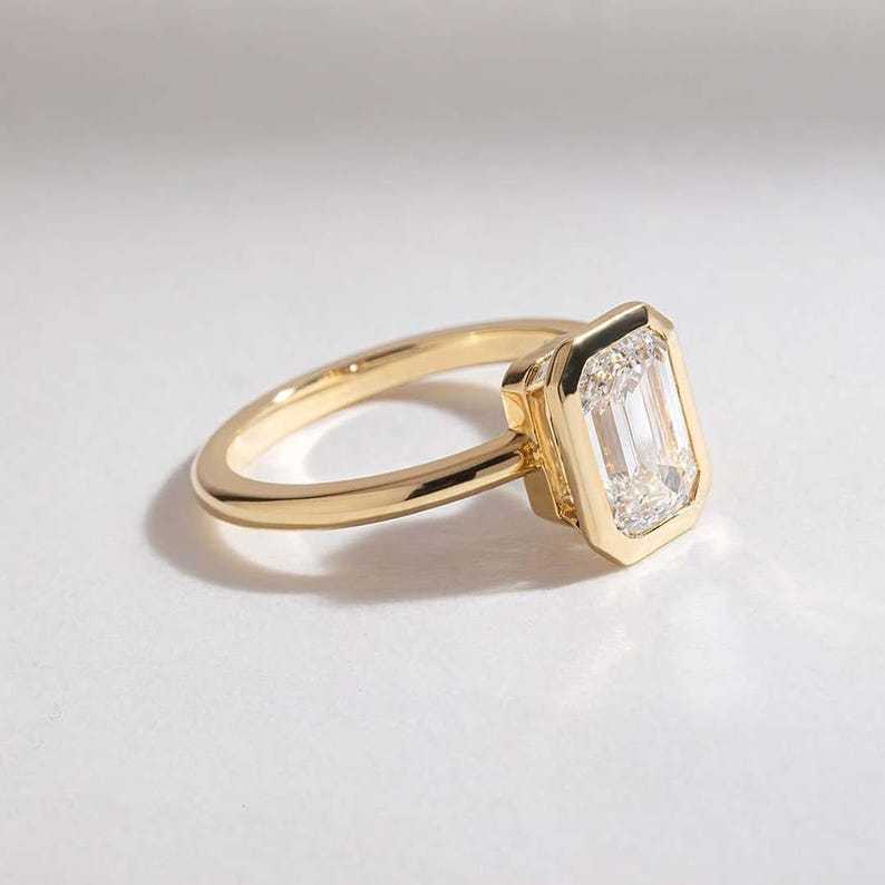 Angled view of a 1.5ct emerald cut lab grown diamond engagement ring in a 14K yellow gold bezel.