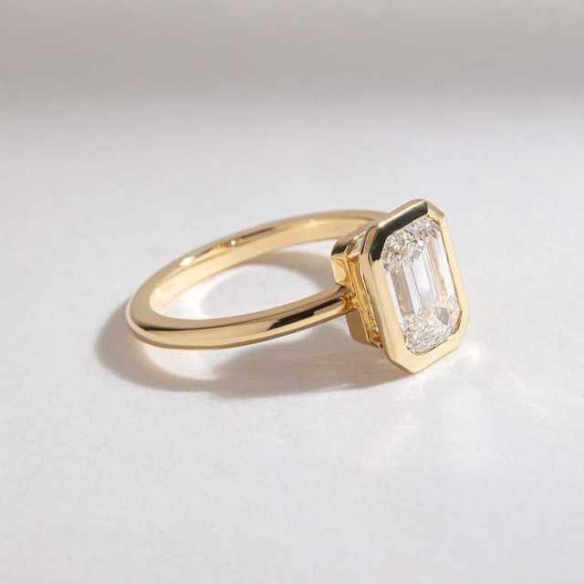 Angled view of a 1.5ct emerald cut lab grown diamond engagement ring in a 14K yellow gold bezel.