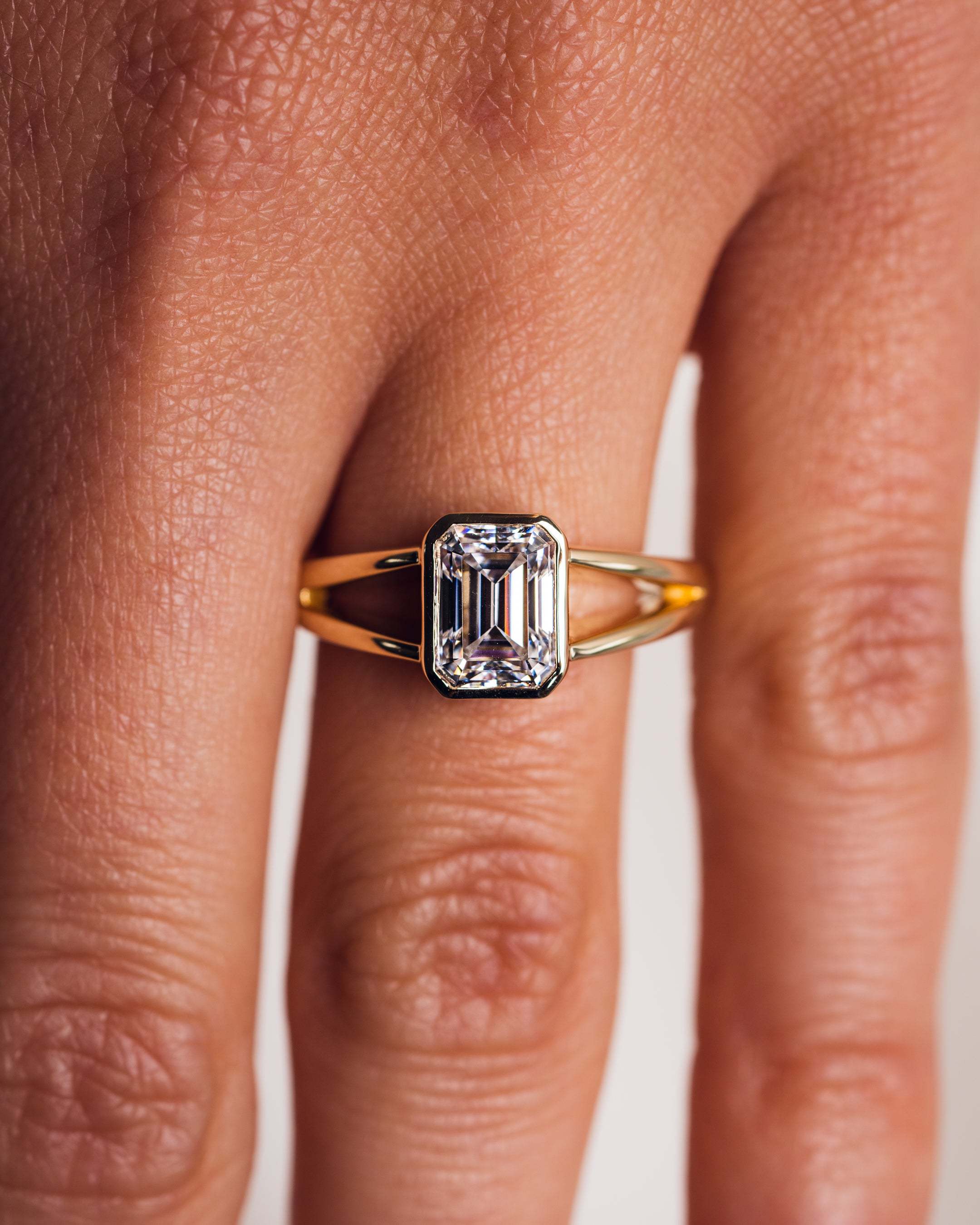 Top-down view of a 14K gold engagement ring featuring a 2 carat emerald cut lab-grown diamond in a full bezel setting.