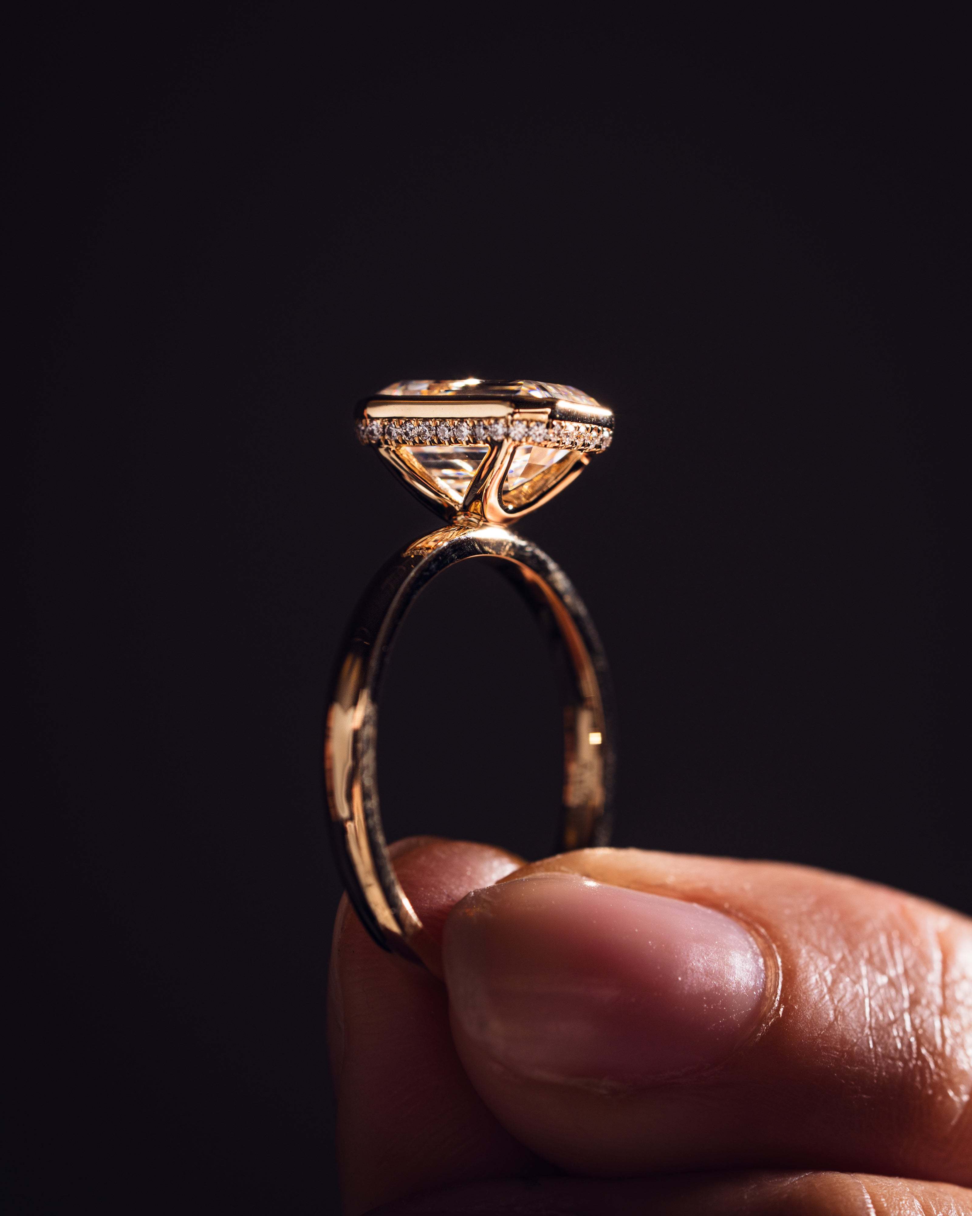 Side profile view of 14K gold bezel engagement ring showing deep step cut pavilion and diamond halo