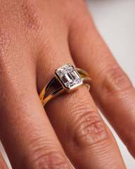 Angled view on a hand showing the split shank band and bezel setting of an emerald cut lab diamond ring in 14K yellow gold.
