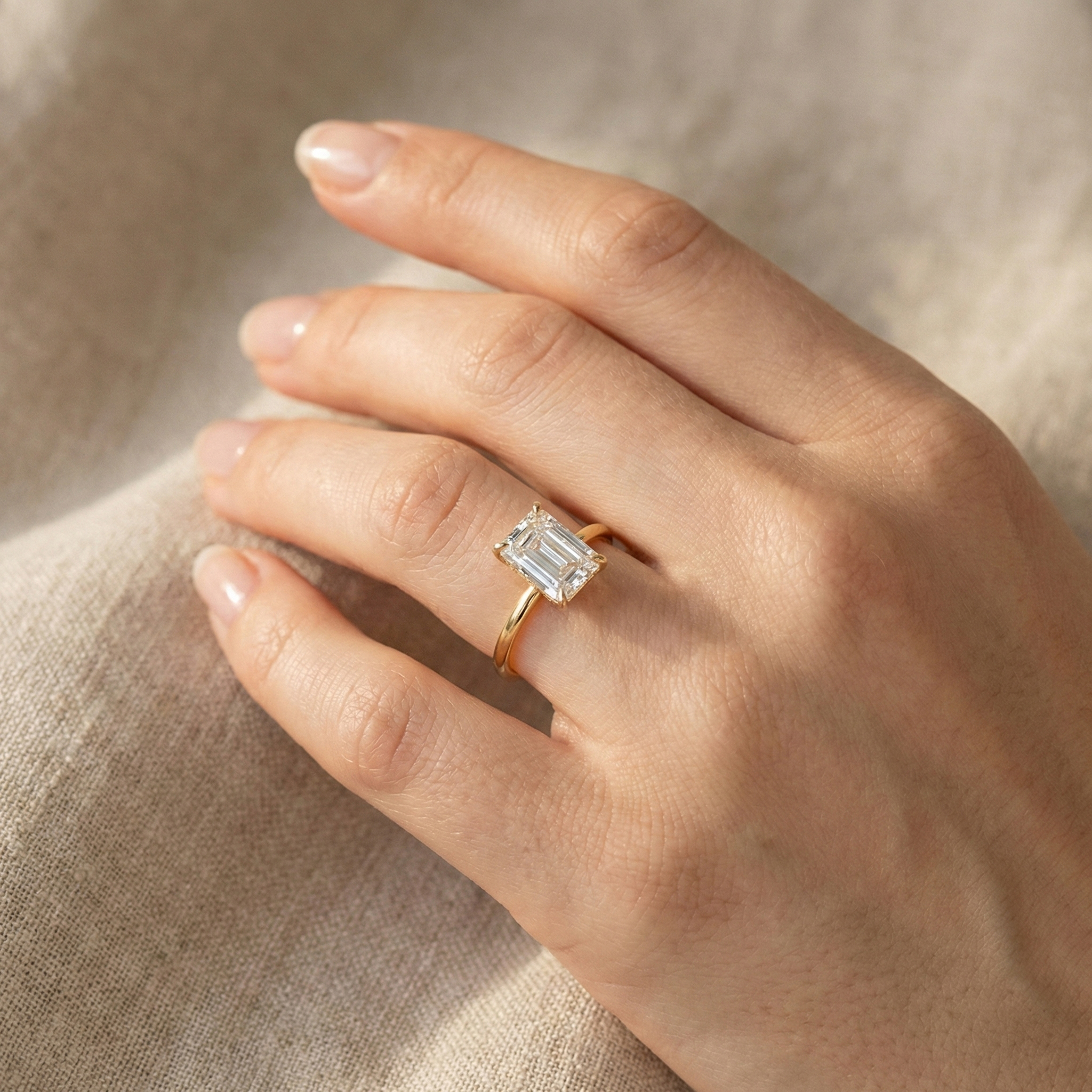 Close-up of a 4-carat E color VS1 clarity emerald cut lab diamond ring worn on a woman's hand against a textured fabric background.