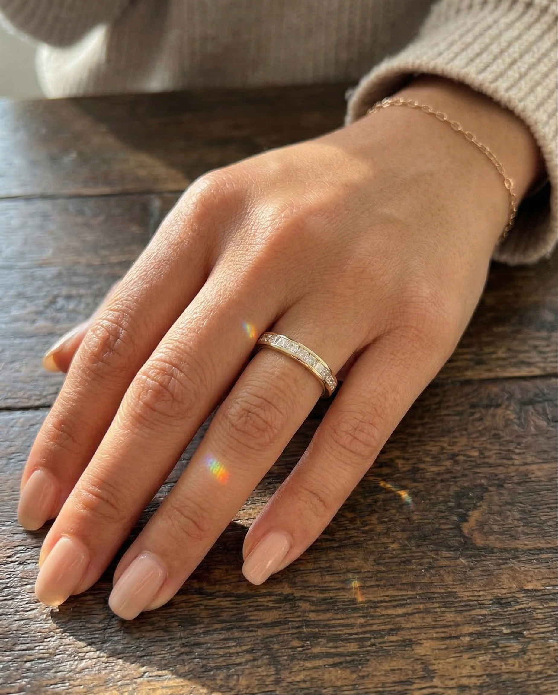 Hand model wearing a brilliant 18K yellow gold channel set lab-grown diamond eternity band, showcasing stunning rainbow fire and princess cut facets.