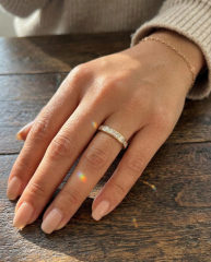 Hand model wearing a brilliant 18K yellow gold channel set lab-grown diamond eternity band, showcasing stunning rainbow fire and princess cut facets.