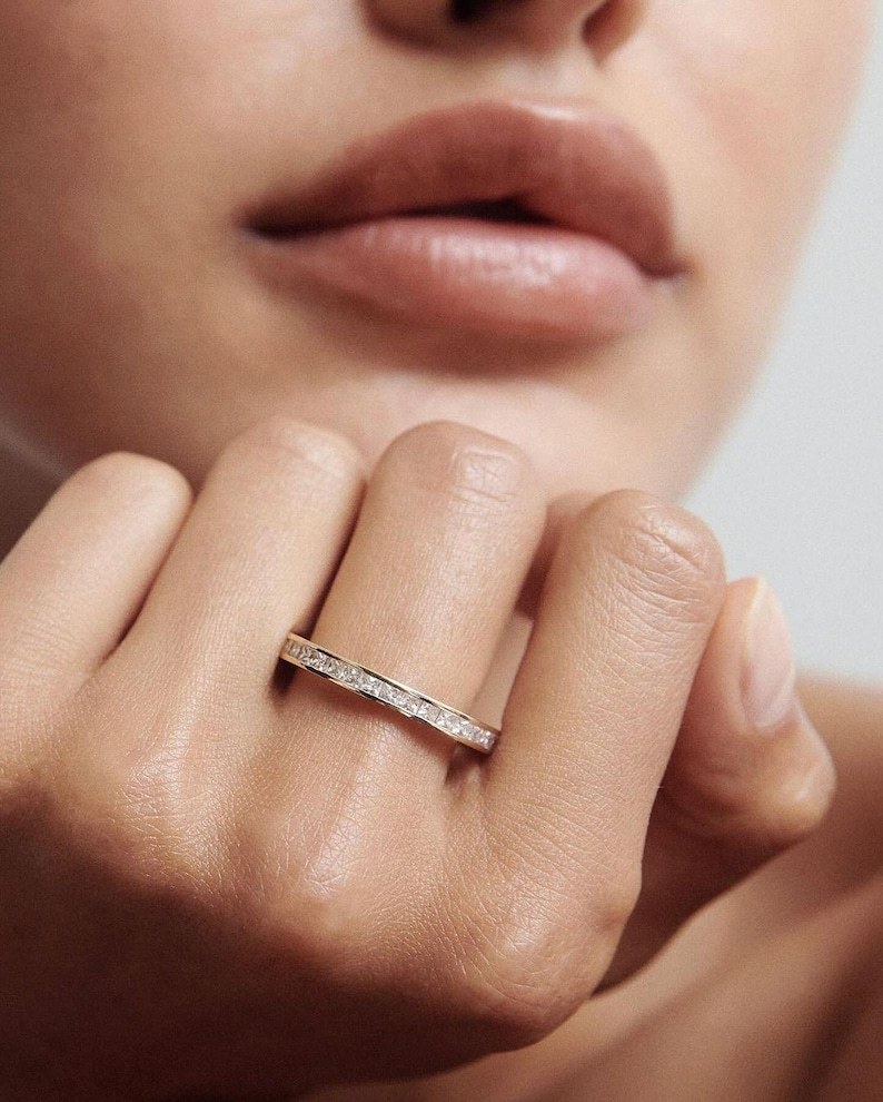 High-fashion close-up of a model resting her face on her hand, elegantly displaying the flawless sparkle of the 18K gold lab-grown diamond eternity ring.