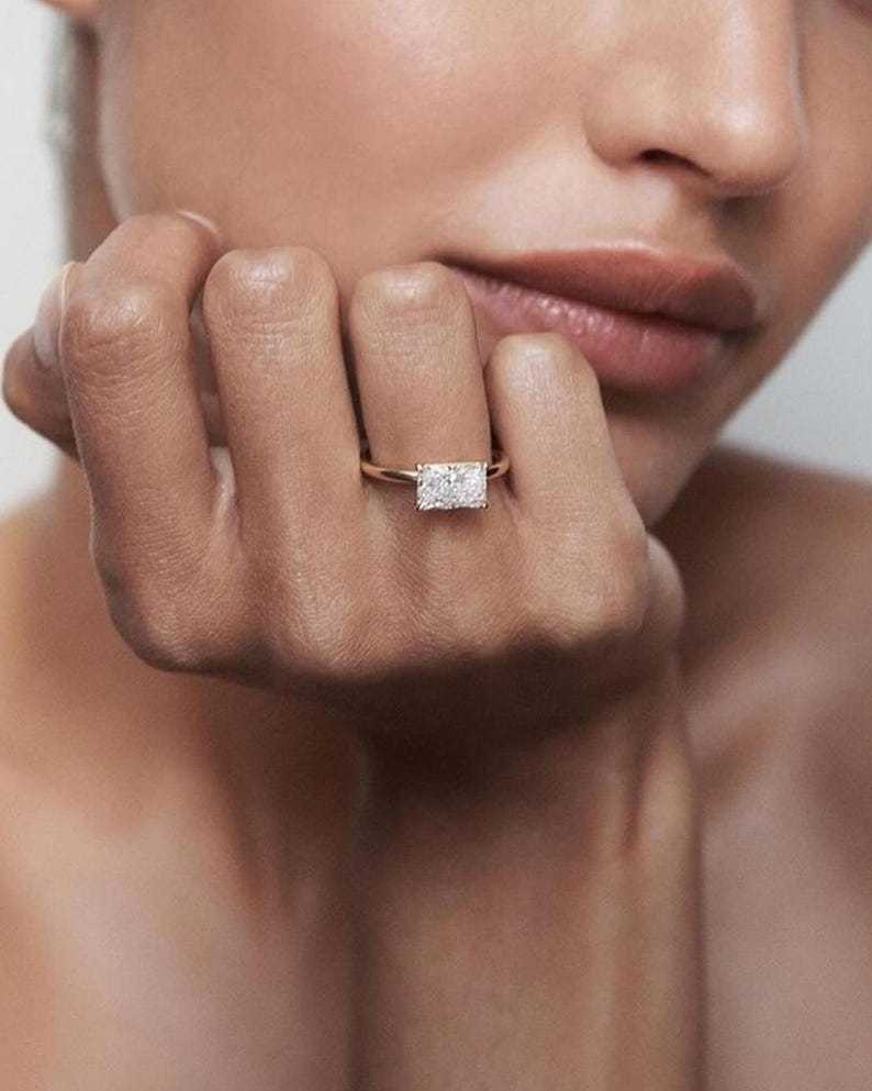 Female model wearing a custom 1.1 carat east-west radiant cut lab diamond engagement ring in 14K gold, emphasizing the extensive horizontal finger coverage and modern minimalist aesthetic of the design.